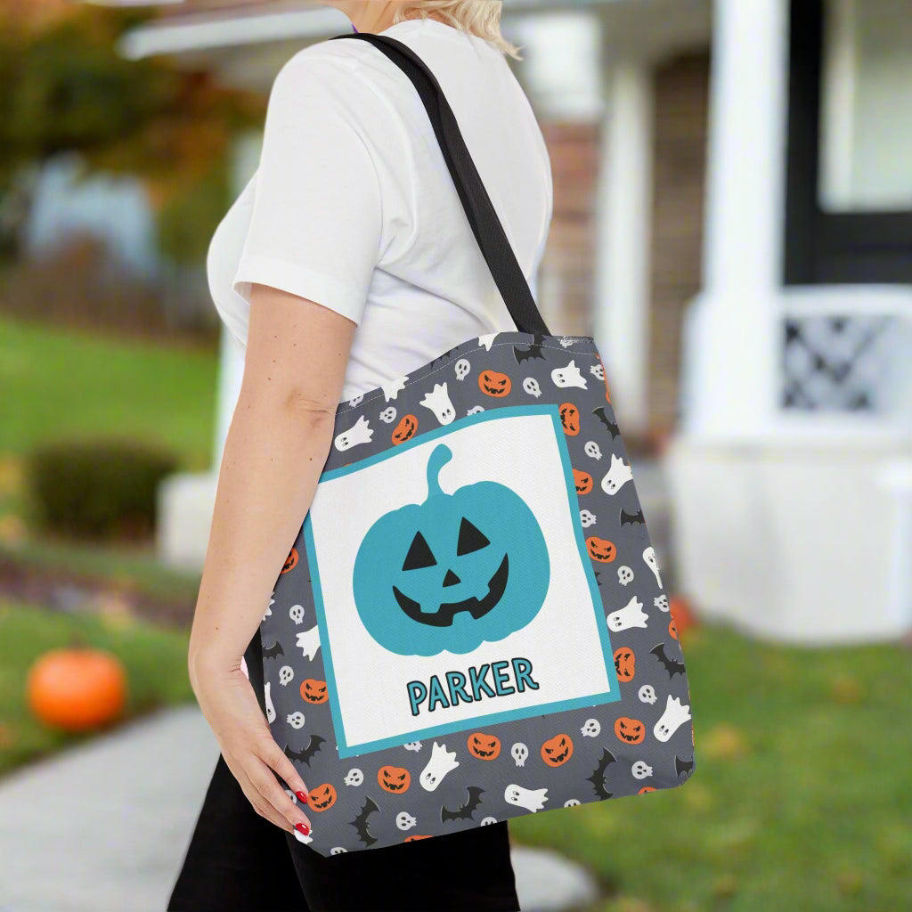 Person holding a Halloween-themed tote bag with a pumpkin design on a pink background with candy decorations.