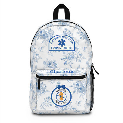 A white backpack with a blue floral pattern, featuring a front pocket with the name 'Charlotte' in blue, a blue emergency medication patch graphic, and a circular peanut allergy badge.
