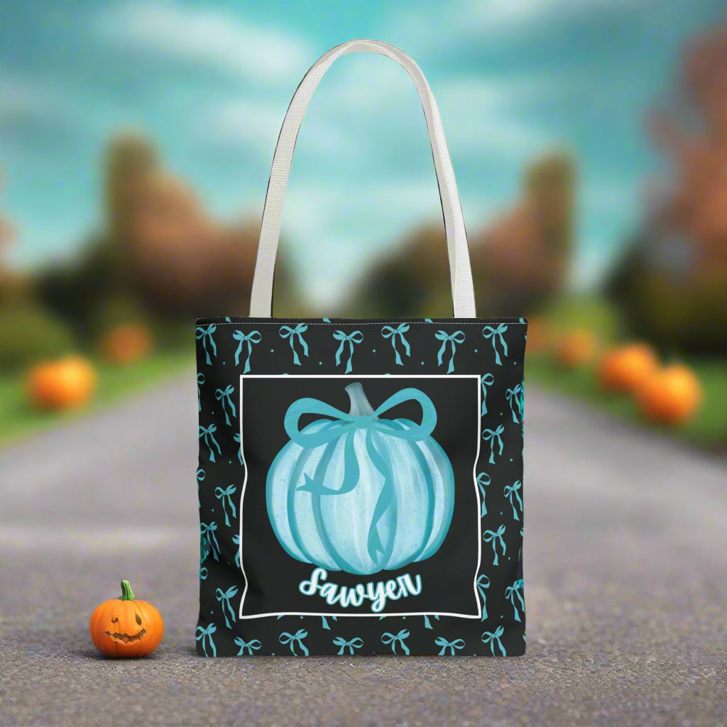 Tote bag with pumpkin design and name on a teal bow background.