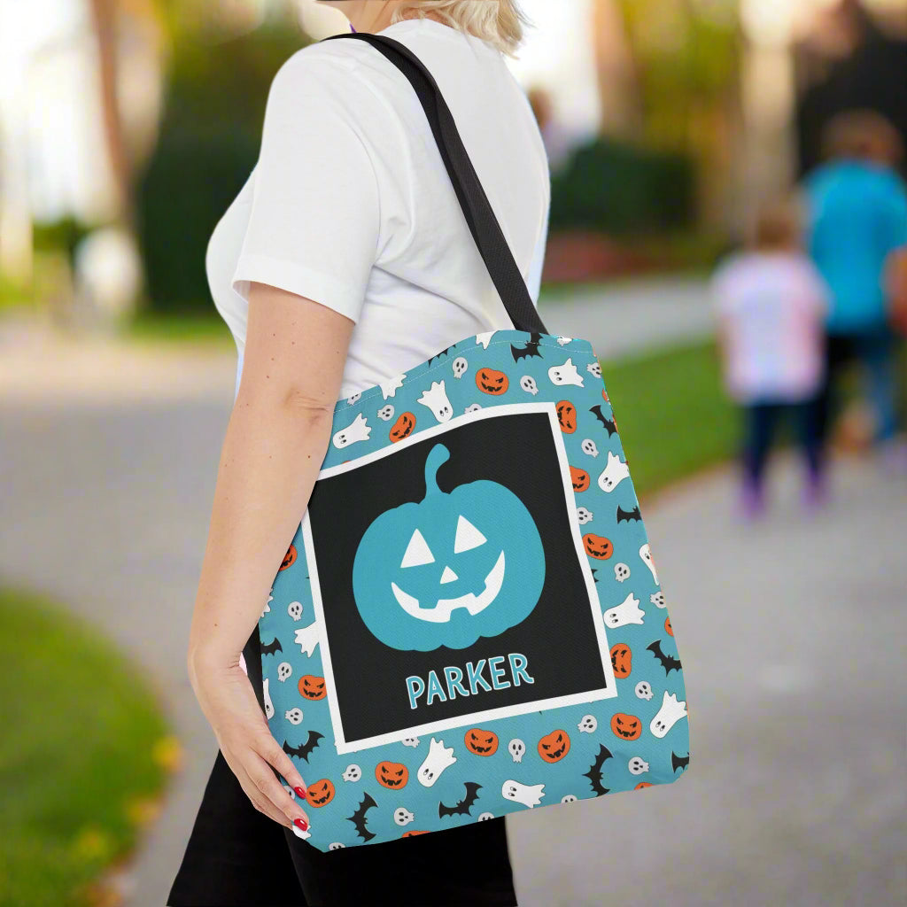 Person holding a Halloween-themed tote bag with a pumpkin design and a name.