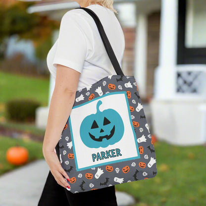 Person holding a Halloween-themed tote bag with a pumpkin design on a pink background with candy decorations.