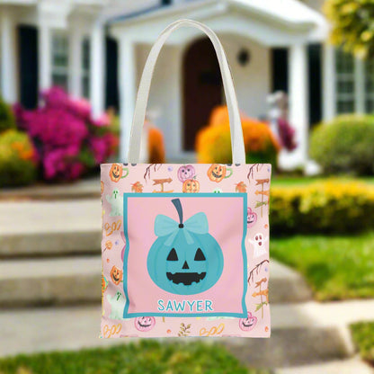 Halloween-themed tote bag with a teal bow pumpkin design and name on a pink and purple pumpkin background.