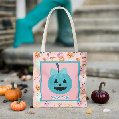 Halloween-themed tote bag with a teal bow pumpkin design and name on a pink background.